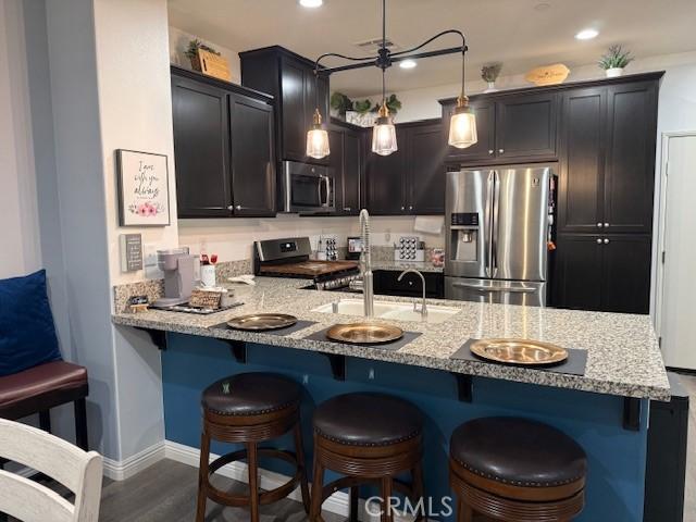16001 Chase Rd Unit 111, Fontana, CA 92336 - kitchen with appliances with stainless steel finishes, light stone countertops, a peninsula, a breakfast bar area, and dark wood finished floors