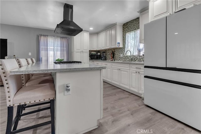 1109 Broadmoor Ave, La Puente, CA 91744 - kitchen with freestanding refrigerator, island range hood, a kitchen bar, light wood-type flooring, and white cabinets
