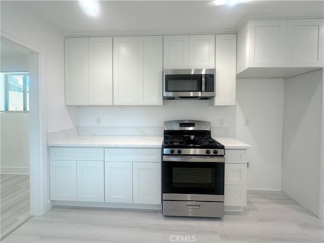 1295 E Whittier Ave, Hemet, CA 92543 - kitchen with stainless steel appliances, white cabinets, light wood-style flooring, and light stone counters