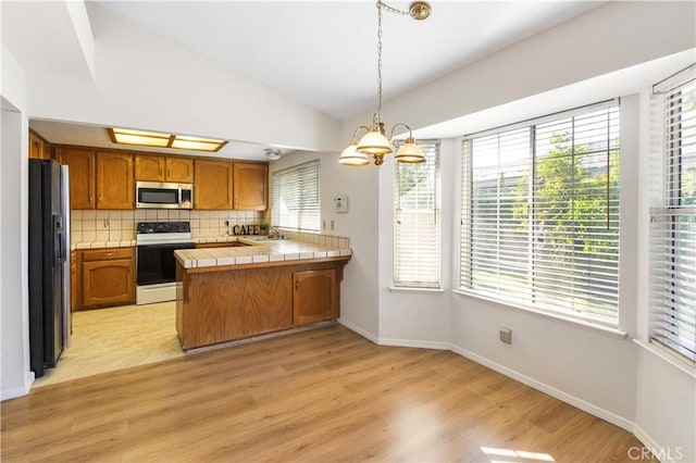 903 San Pablo Ave, Merced, CA 95348 - kitchen with white range with electric cooktop, stainless steel microwave, a peninsula, vaulted ceiling, and brown cabinets