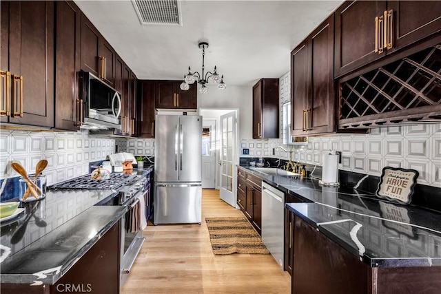 68613 E St, Cathedral City, CA 92234 - kitchen with appliances with stainless steel finishes, light wood-style flooring, decorative backsplash, dark brown cabinetry, and dark stone countertops