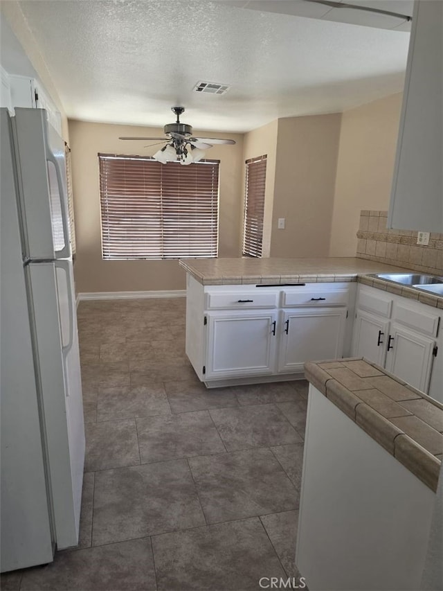 15171 San Jose Dr, Victorville, CA 92394 - kitchen featuring freestanding refrigerator, a peninsula, ceiling fan, white cabinetry, and a textured ceiling