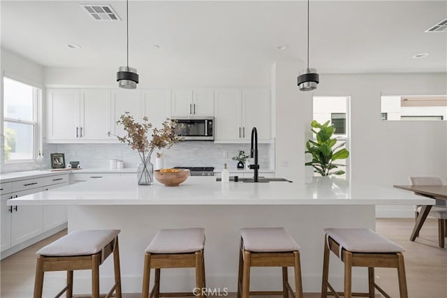 687 W 17th St, Costa Mesa, CA 92627 - kitchen with stainless steel microwave, decorative backsplash, white cabinetry, and recessed lighting