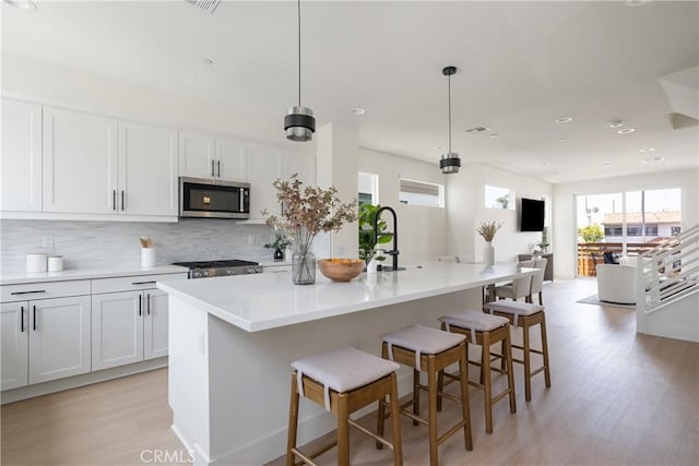 687 W 17th St, Costa Mesa, CA 92627 - kitchen featuring stainless steel microwave, light wood finished floors, decorative backsplash, a kitchen bar, and a kitchen island with sink