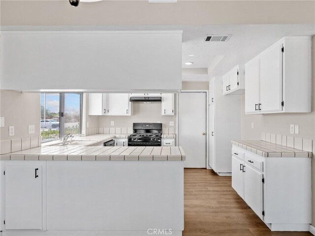 17702 Hinton St, Hesperia, CA 92345 - kitchen featuring gas range oven, a peninsula, wood finished floors, white cabinetry, and tile counters