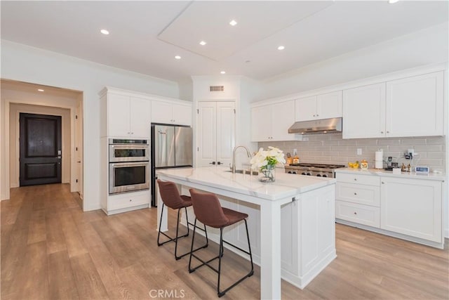 50 Tollson, Irvine, CA 92620 - kitchen featuring appliances with stainless steel finishes, under cabinet range hood, a breakfast bar, white cabinetry, and decorative backsplash