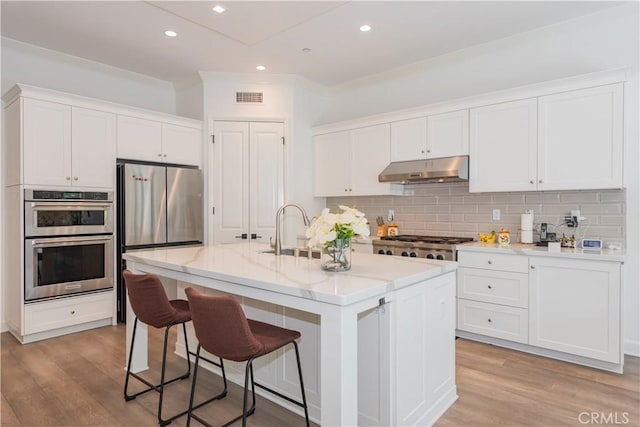 50 Tollson, Irvine, CA 92620 - kitchen featuring under cabinet range hood, stainless steel appliances, white cabinetry, a kitchen breakfast bar, and decorative backsplash