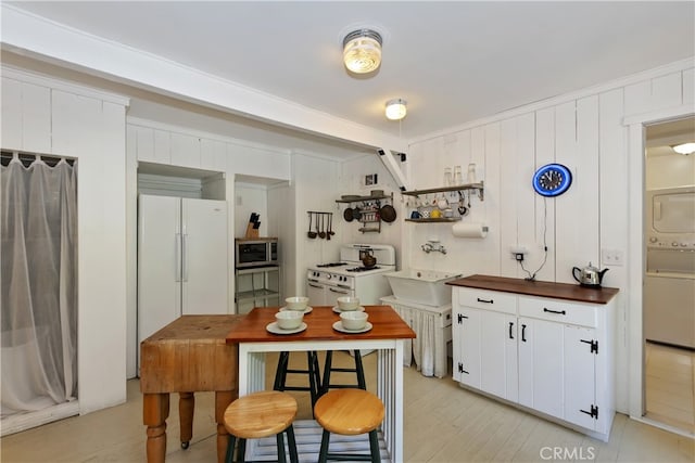 425 Blue Jay Canyon Rd, Blue Jay, CA 92317 - kitchen with white appliances, stacked washer / dryer, white cabinetry, open shelves, and light wood finished floors