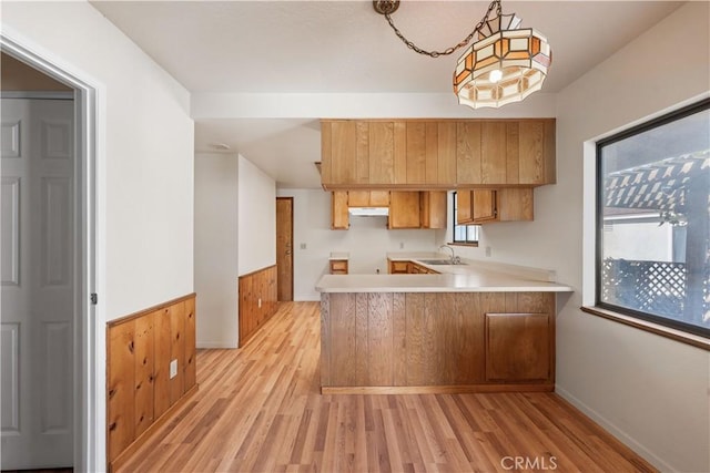 14526 Hardtree Dr, Lake Hughes, CA 93532 - kitchen with light wood-style floors, brown cabinets, light countertops, a peninsula, and wainscoting