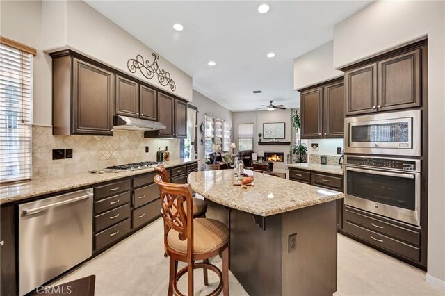 28089 Promontory Ln, Valencia, CA 91354 - kitchen with appliances with stainless steel finishes, ceiling fan, dark brown cabinetry, a kitchen bar, and a kitchen island