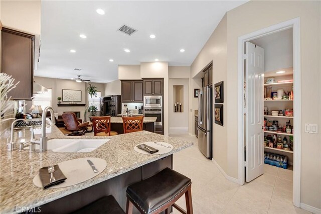 28089 Promontory Ln, Valencia, CA 91354 - kitchen featuring stainless steel appliances, a peninsula, a breakfast bar, light stone countertops, and dark brown cabinets