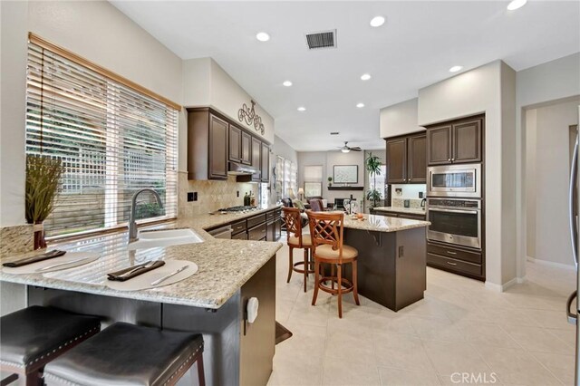 28089 Promontory Ln, Valencia, CA 91354 - kitchen featuring stainless steel appliances, a breakfast bar area, dark brown cabinetry, light stone counters, and recessed lighting