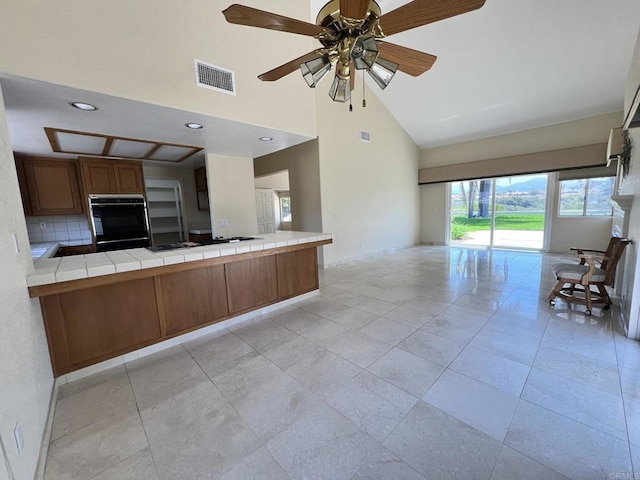 14109 Arbolitos Dr, Poway, CA 92064 - kitchen featuring black oven, open floor plan, high vaulted ceiling, tile countertops, and brown cabinetry