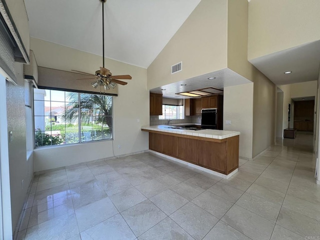 14109 Arbolitos Dr, Poway, CA 92064 - kitchen with black oven, a peninsula, a ceiling fan, high vaulted ceiling, and tile counters