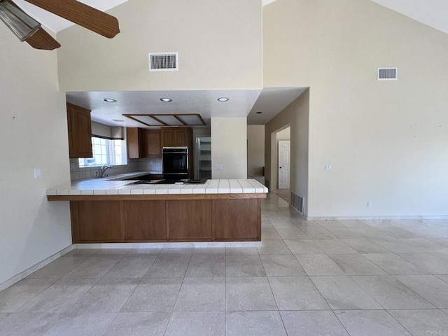 14109 Arbolitos Dr, Poway, CA 92064 - kitchen with high vaulted ceiling, tile counters, black appliances, a peninsula, and backsplash