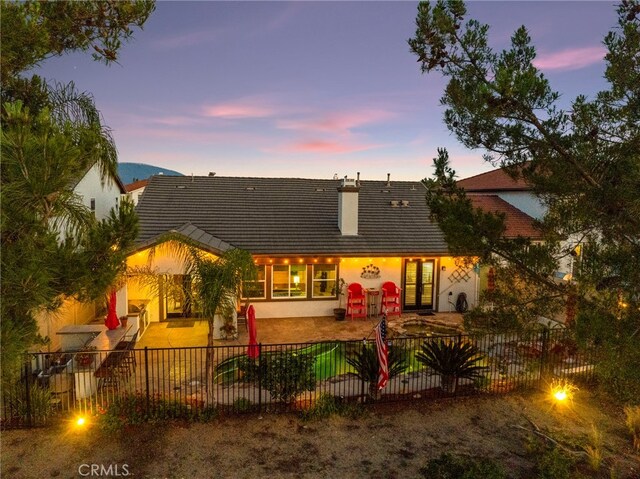 32872 Northshire Cir, Temecula, CA 92592 - back of house at dusk featuring a fenced backyard, a patio area, a tiled roof, stucco siding, and french doors