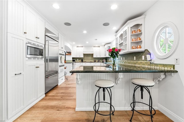 2726 Cardinal Dr, Costa Mesa, CA 92626 - kitchen featuring built in appliances, a peninsula, backsplash, white cabinets, and custom range hood