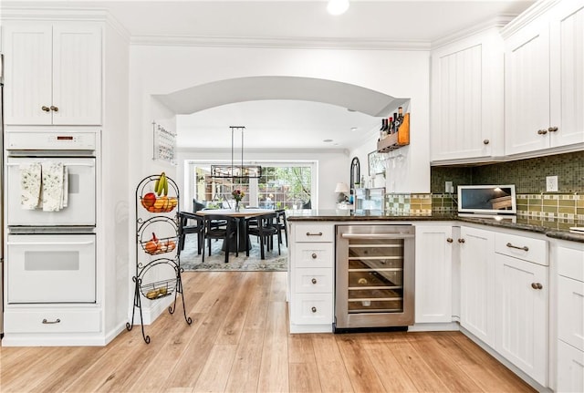2726 Cardinal Dr, Costa Mesa, CA 92626 - kitchen with wine cooler, double oven, white cabinets, a peninsula, and decorative backsplash