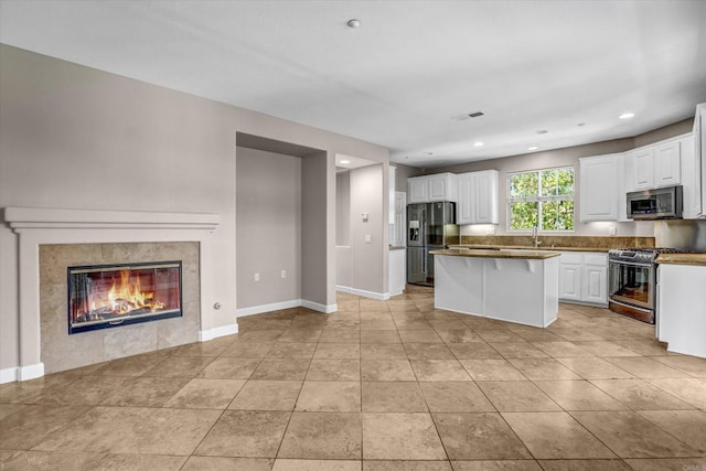 13325 Via Tresca Unit 7, San Diego, CA 92129 - kitchen featuring stainless steel appliances, a kitchen island, white cabinetry, a tiled fireplace, and recessed lighting