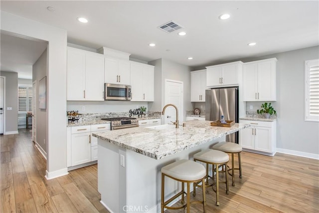 1563 Sunswept Way, Beaumont, CA 92223 - kitchen featuring stainless steel appliances, a kitchen breakfast bar, light wood finished floors, a center island with sink, and white cabinetry
