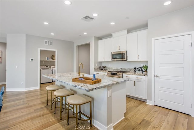 1563 Sunswept Way, Beaumont, CA 92223 - kitchen with stainless steel appliances, washing machine and clothes dryer, light wood-style flooring, a breakfast bar, and recessed lighting