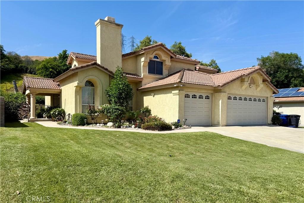 25961 Brookmere Ave, Loma Linda, CA 92354 - mediterranean / spanish house featuring a chimney, an attached garage, stucco siding, a front lawn, and driveway