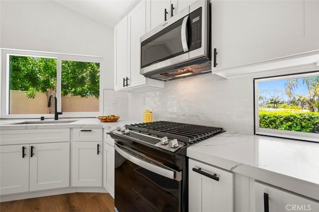 4 Saint Martin, Laguna Niguel, CA 92677 - kitchen featuring appliances with stainless steel finishes, lofted ceiling, backsplash, light stone counters, and white cabinetry