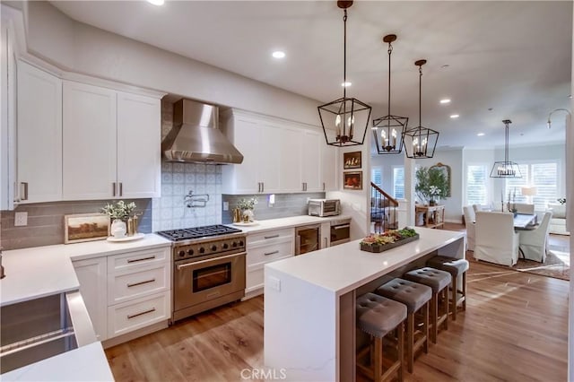 2424 Gird Rd, Fallbrook, CA 92028 - kitchen featuring wall chimney range hood, stainless steel range, a kitchen bar, white cabinetry, and light countertops