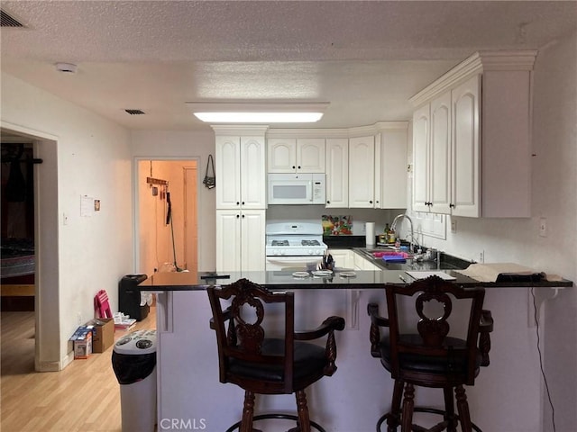 35590 Santa Fe St, Daggett, CA 92327 - kitchen with white appliances, a peninsula, light wood-style floors, white cabinets, and dark countertops
