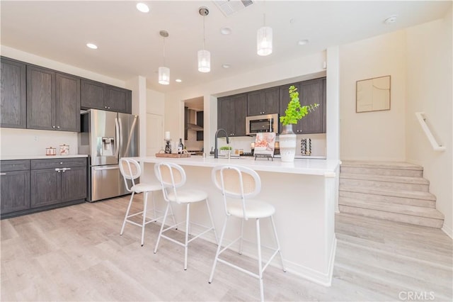 1504 Granada Rd, Upland, CA 91786 - kitchen with appliances with stainless steel finishes, light wood-style floors, dark brown cabinets, a breakfast bar area, and hanging light fixtures