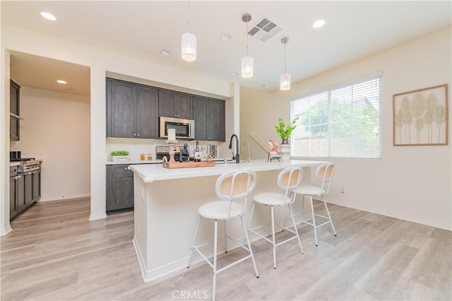 1504 Granada Rd, Upland, CA 91786 - kitchen featuring stainless steel appliances, light wood-style flooring, a kitchen bar, light countertops, and an island with sink