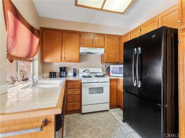 16873 Silica Dr, Victorville, CA 92395 - kitchen with freestanding refrigerator, white gas range, under cabinet range hood, tile counters, and brown cabinets
