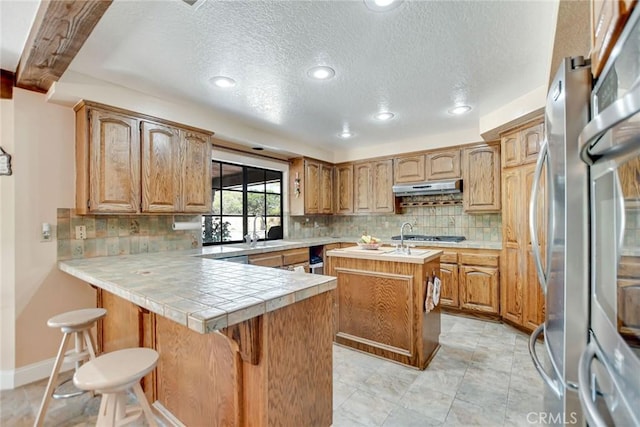 1013 Idaho Ct, Claremont, CA 91711 - kitchen featuring under cabinet range hood, an island with sink, tasteful backsplash, a kitchen bar, and recessed lighting