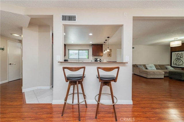1068 Richmond Dr, Claremont, CA 91711 - kitchen with wood finished floors, a breakfast bar area, a textured ceiling, light countertops, and pendant lighting