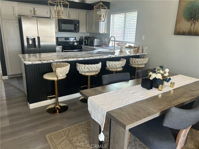 2258 El Rio St, Lancaster, CA 93535 - kitchen featuring stainless steel appliances, a peninsula, wood finished floors, a breakfast bar, and decorative light fixtures