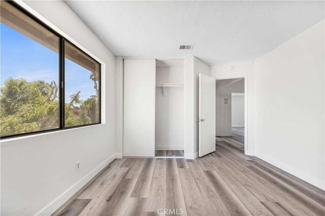 14225 Woodpark Dr, Moreno Valley, CA 92553 - unfurnished bedroom with light wood finished floors, a textured ceiling, multiple windows, and a closet