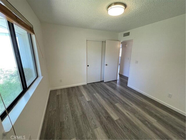 1935 W Santa Ana Ave, Fresno, CA 93705 - unfurnished bedroom featuring a textured ceiling, multiple windows, dark wood finished floors, and a closet