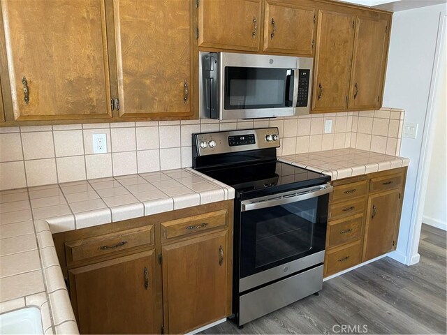 1935 W Santa Ana Ave, Fresno, CA 93705 - kitchen featuring appliances with stainless steel finishes, wood finished floors, backsplash, brown cabinetry, and tile countertops