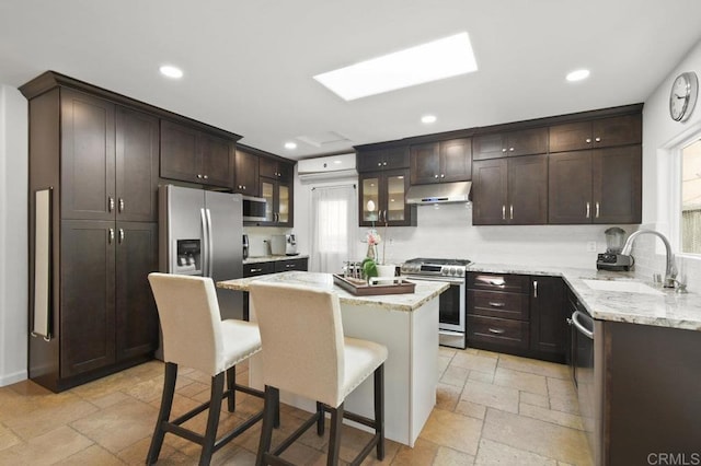 6038 Bradford St, San Diego, CA 92115 - kitchen featuring appliances with stainless steel finishes, under cabinet range hood, stone tile flooring, dark brown cabinets, and a kitchen bar