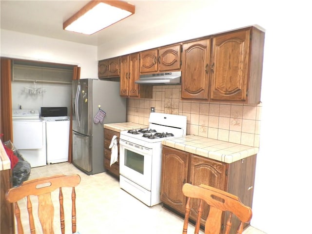 662 Kempton Ave, Monterey Park, CA 91755 - kitchen with white range with gas cooktop, washing machine and clothes dryer, under cabinet range hood, stainless steel fridge, and tile countertops
