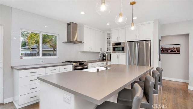 5202 E Conant St, Long Beach, CA 90808 - kitchen featuring wall chimney exhaust hood, appliances with stainless steel finishes, wood finished floors, an island with sink, and a breakfast bar