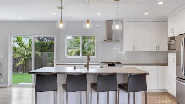 5202 E Conant St, Long Beach, CA 90808 - kitchen with wall chimney exhaust hood, recessed lighting, white cabinetry, light wood finished floors, and decorative backsplash