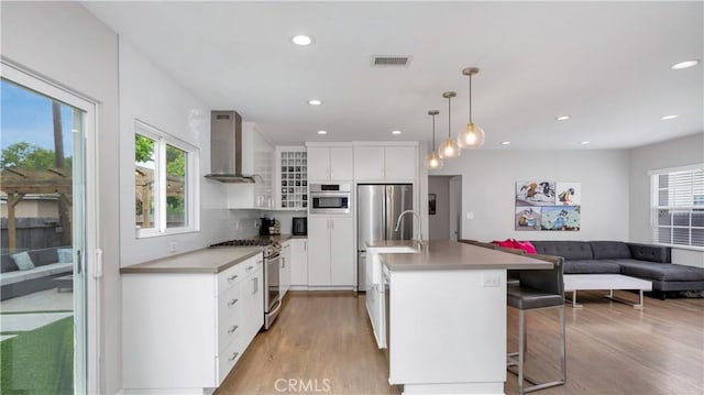 5202 E Conant St, Long Beach, CA 90808 - kitchen with stainless steel appliances, wall chimney range hood, light wood-style floors, recessed lighting, and white cabinets