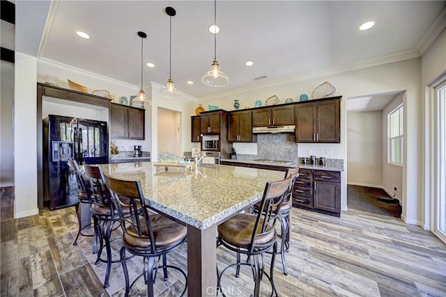 35115 Mahogany Glen Dr, Winchester, CA 92596 - kitchen with stainless steel appliances, under cabinet range hood, dark brown cabinets, ornamental molding, and a large island