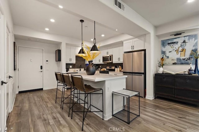 9384 Calm Water Pl, Rancho Cucamonga, CA 91730 - kitchen featuring appliances with stainless steel finishes, a breakfast bar, white cabinets, recessed lighting, and wood finished floors