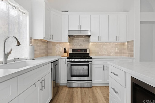 1642 Marbella Dr, Vista, CA 92081 - kitchen with appliances with stainless steel finishes, under cabinet range hood, wine cooler, white cabinets, and light wood finished floors