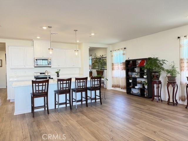 7676 Nectarsweet Dr, Riverside, CA 92507 - kitchen featuring appliances with stainless steel finishes, wood finished floors, light countertops, white cabinetry, and a breakfast bar