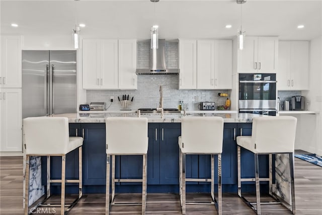1954 Shipway Ave, Long Beach, CA 90815 - kitchen featuring wall chimney exhaust hood, appliances with stainless steel finishes, dark wood-style flooring, decorative backsplash, and a center island with sink