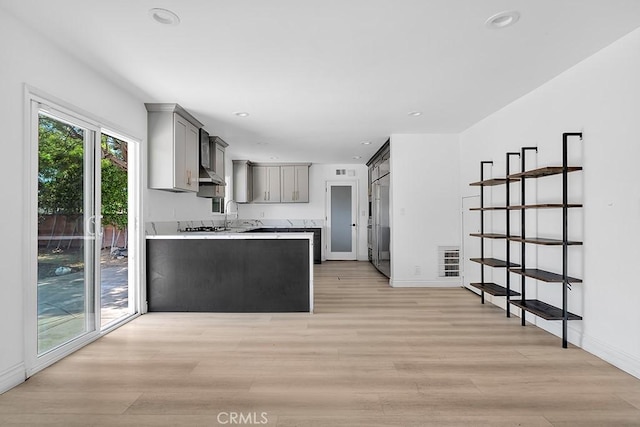 7812 Fairchild Ave, Winnetka, CA 91306 - kitchen featuring gray cabinetry, light wood finished floors, a peninsula, light countertops, and under cabinet range hood
