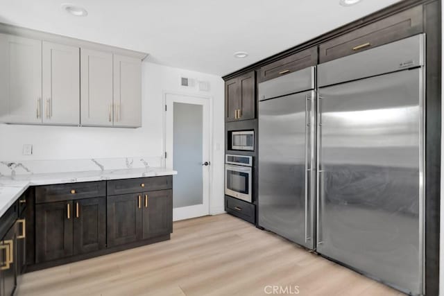 7812 Fairchild Ave, Winnetka, CA 91306 - kitchen featuring built in appliances, light wood-style flooring, light stone counters, dark brown cabinetry, and recessed lighting